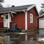 Fritidshus i röd färg med vit trim vid snötäckt tomt och istappar.